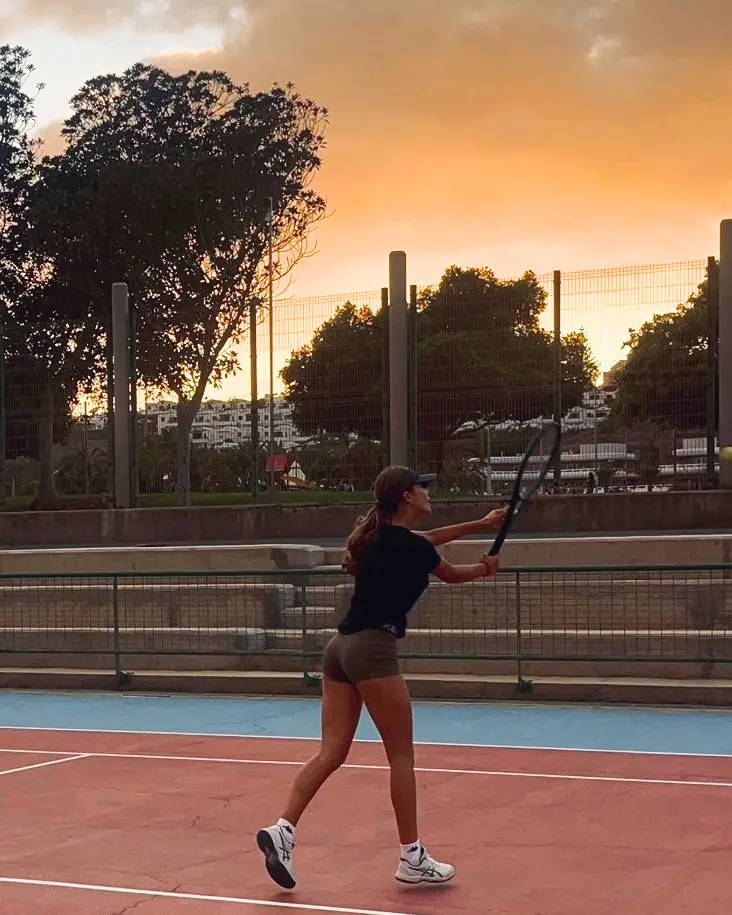 Nicole termina un golpe en una pista dura al atardecer, bajo un cielo naranja.